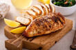 © fahrwasser - Grilled chicken breast whole and sliced on a cutting board with lemon
