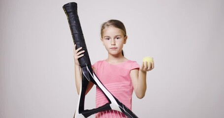 Wall Mural - Young female tennis player with big oversize racket smiling. Girl posing in pink sports outfit and holging a ball in her hand.