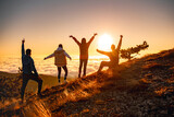 Fototapeta  - Group of happy friends are standing at mountain top and greeting sunrise or sunset above clouds
