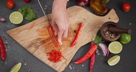 Wall Mural - Woman cutting red hot chili pepper on a wooden cutting board at domestic kitchen