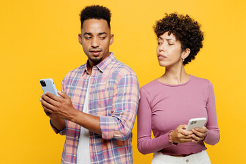 Wall Mural - Young sad couple two friend family man woman of African American ethnicity wear purple casual clothes together wife try to look at husband mobile cell phone isolated on plain yellow orange background