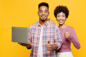 Wall Mural - Young happy couple two friends family IT man woman wear purple casual clothes together hold use work on laptop pc computer browsing internet show thumb up isolated on plain yellow orange background.