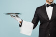 © ViDi Studio - Cropped close up adult barista male waiter butler man wear shirt black suit bow tie uniform hold in hand metal tray plate work at cafe isolated on plain blue background. Restaurant employee concept.