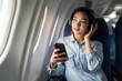 © Natee Meepian - Young female listening song during flight in first class cabin using smartphone, woman entertain on airplane board enjoy music in headphone from smartphone