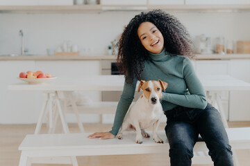 Sticker - Smiling woman in turtleneck with her dog at a kitchen table, radiating joy.