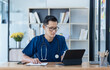 © SOMKID - Asian male doctor with patient clipboard and laptop computer sitting at desk in hospital, Medicine and healthcare concept.