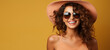 Joyful woman with curly hair, sunglasses, and straw hat exudes summer vibes on a yellow background