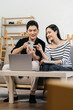 © NINENII - Asian couple relaxing with smartphone at home, loving man and woman sitting on couch together, Browsing Internet on mobile phone and laptop.
