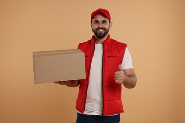 Canvas Print - Happy young courier with parcel showing thumb up on light brown background