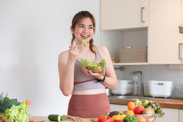 Healthy Asian woman takes care of her health by eating vegetable and fruit salad, adding vitamins in the kitchen.