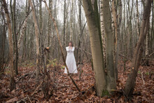 art portrait of woman in white dress standing alone in forest with fallen leaves 