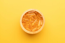 Oil Softgel Capsules In Wooden Bowl On Yellow Background. Nutritional Supplement Contains Fish Oil, Omega 3, Omega 6, Omega 9, Vitamin E, Vitamin D And Vitamin A. Top View.