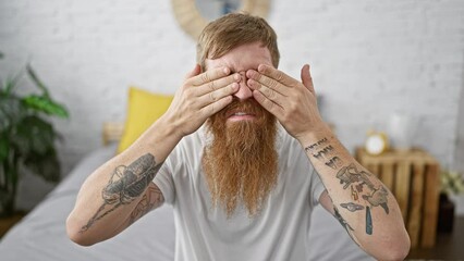 Wall Mural - Exhausted young redhead man yawning hard, seated in bedroom, trying to wake up and start the morning