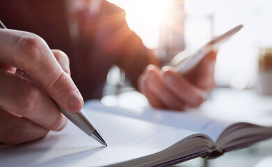 Wall Mural - Close up of woman's hands writing in spiral notepad placed on wooden desktop with various items