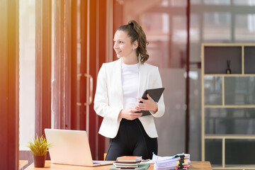 A young woman cheerful smiling standing and holding digital tablet In the office room.