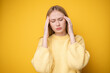 © deine_liebe - Portrait of a cute girl suffering from a headache on a yellow background. Young woman suffering from migraine.