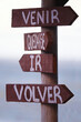 quatro setas de madeira presas a um poste indicando caminhos simbólicos ou escolhas onde se le em espanhol: venir, quedarse, ir, volver