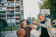 © Marko Geber - Grandfather teaching his grandson how to play basketball at an outdoor basketball court