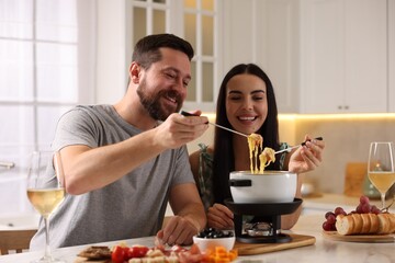 Poster - Affectionate couple enjoying cheese fondue during romantic date in kitchen