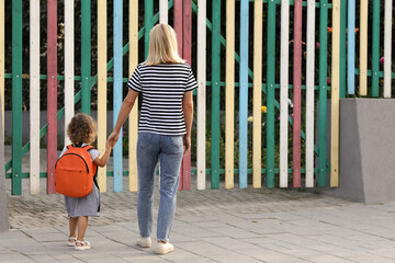 Sticker - Woman and her little daughter on their way to kindergarten outdoors, back view. Space for text