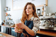 Portrait of a smiling female barista with a takeaway drink standing behind a bar counter. Business concept, food and drinks.