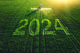 Fototapeta Na sufit - 2024 Happy New Year concept and Aerial view of farming tractor plowing and spraying on field.