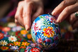 Close-up of hands delicately painting an Easter egg with folk designs.