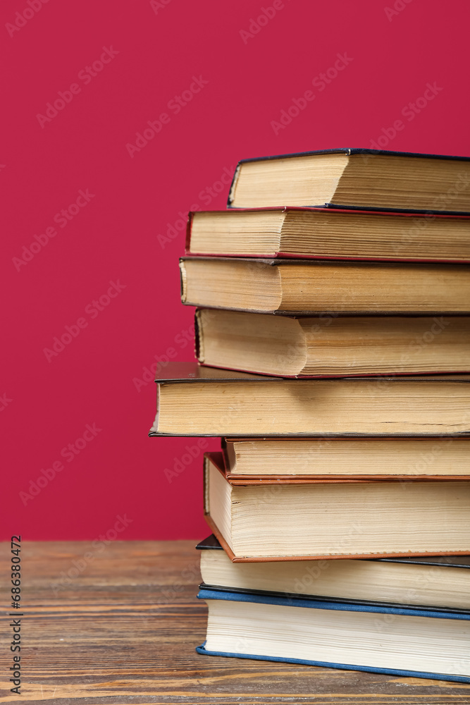 Stack of books on wooden table against red background