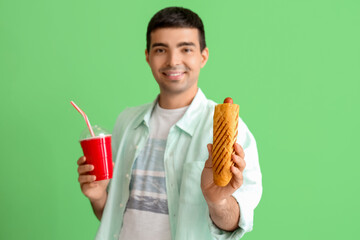 Wall Mural - Happy young man with tasty french hot dog and drink on green background