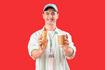 Wall Mural - Young man with tasty hot dog and cup of coffee on red background