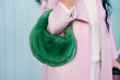© okrasiuk - Close up cropped stylish woman in pink coat holding bright green fluffy fur bag in her hands. Fashionable modern green faux fur bag. Winter street fashion. Selective focus.