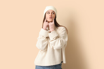 Canvas Print - Young woman in winter clothes blowing kiss on beige background