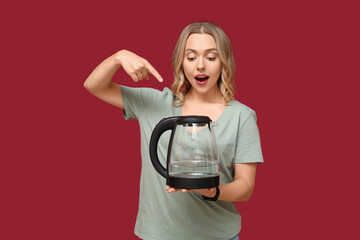 Wall Mural - Surprised young woman pointing at modern electric kettle on red background