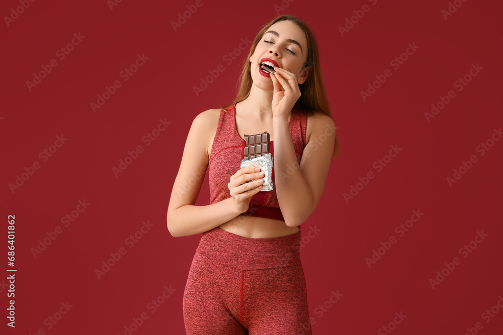 Young woman eating sweet chocolate bar on red background