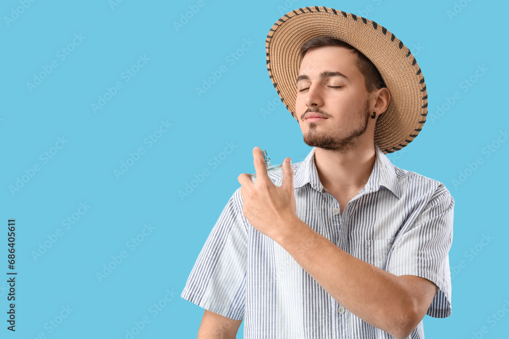 Young man in straw hat with perfume on blue background