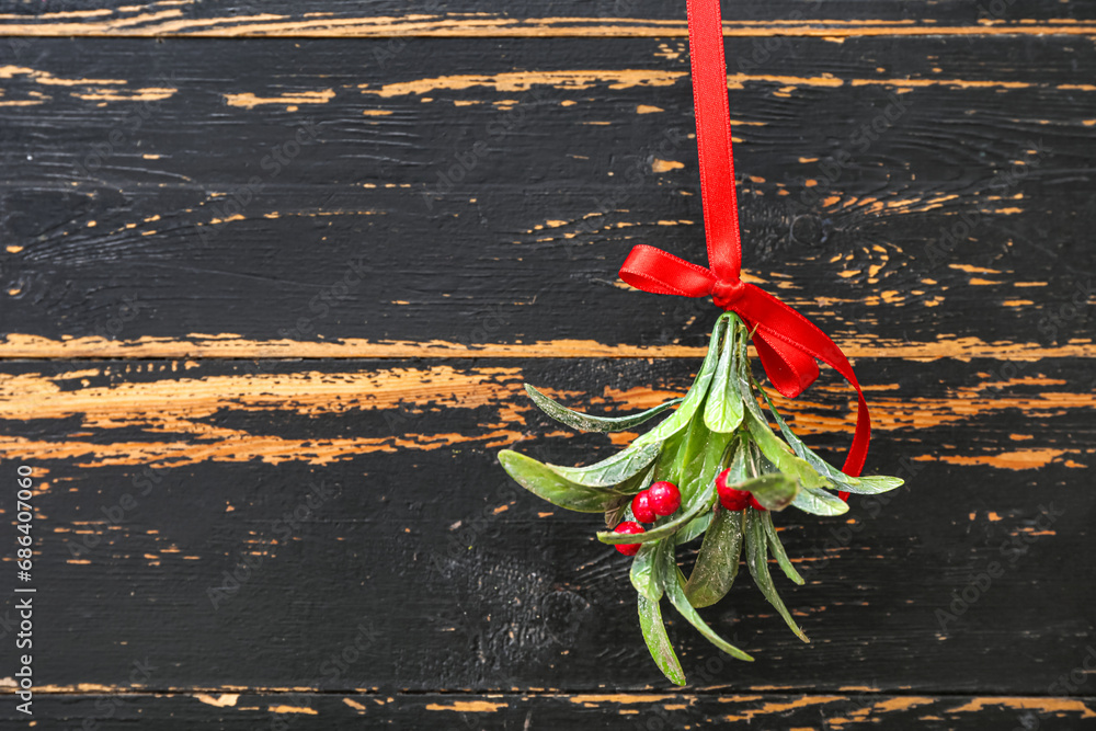 Mistletoe branch with ribbon on dark wooden background