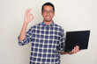 © KrishnaTedjo - Adult Asian man smiling and give OK finger sign while holding a laptop