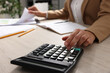 © New Africa - Woman using calculator while working with document at wooden table, closeup