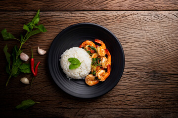 Canvas Print - Stir-fried shrimp with basil Thai street food arranged on a black plate Spicy Thai food placed on a wooden table. Top view.