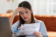 © 220 Selfmade studio - Young Asian woman looks stressed while examining a bill, impactful financial pressure, anxiety, and the challenges of managing expenses. Financial problem.