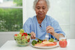 © manassanant - Asian elderly woman patient eating salmon stake and vegetable salad for healthy food in hospital.