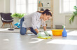 © Studio Romantic - Happy housewife cleaning the floor at home. Young woman in rubber gloves washing and wiping light gray wooden or laminate flooring in the living room. Housework concept