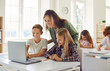 © Studio Romantic - Happy school children using a laptop in the classroom. Cheerful schoolboy and schoolgirl together with their friendly teacher looking at the notebook computer and smiling. Technology education concept