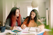 © Maskot - Woman assisting daughter in doing homework while sitting at table