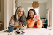 © Maskot - Happy grandmother and granddaughter using smart phone at home
