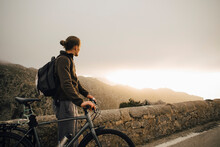 Side View Of Young Man Looking At Mountains While Standing With Bicycle On Road