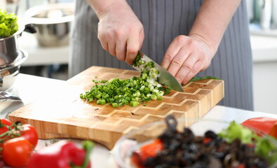 Wall Mural - Closeup of hands of cook holding knife for cutting green onions. Sliced fresh green onions and cooking vegetables in kitchen