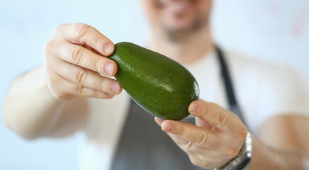 Wall Mural - Male cook holds green fresh tasty avocado in hands. Natural fresh organic exotic fruits and healthy food concept