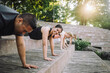 © Maskot - Portrait of smiling woman doing push-ups with friends on steps at park