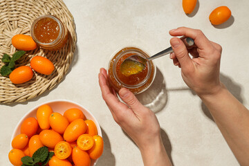 Sticker - Kumquat in bowl, jars with jam and hands on light background, top view